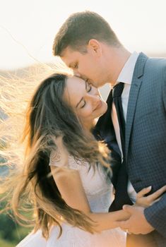 Groom kisses the temple of bride with her hair flying in the wind. High quality photo