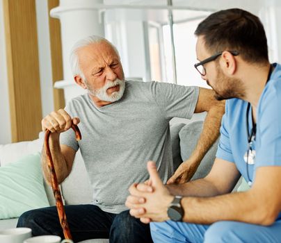 Doctor or nurse caregiver help senior man in pain at home or nursing home
