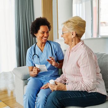 Doctor or nurse caregiver showing a prescrption drug bottle to senior woman at home or nursing home