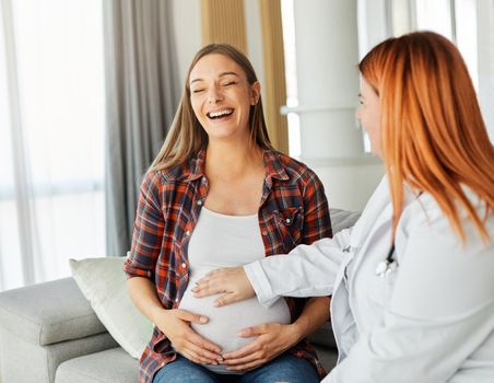 Portrait of a young happy pregnant woman doing exam with doctor or nurse during a visit at home or in a clinic