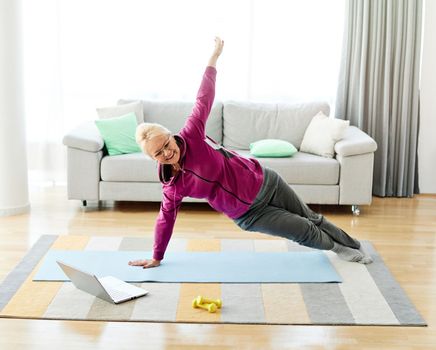 Senior woman exercise stretching yoga using laptop online instructions at home health care