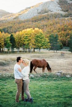 Man kisses woman on the forehead on a green lawn next to a grazing horse. High quality photo