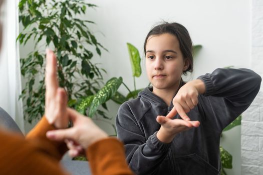 Cute little girl make hand gesture learning sign language with mom or female nanny, smiling small kid practice nonverbal talk with teacher at home, preschooler disabled child have lesson with tutor.