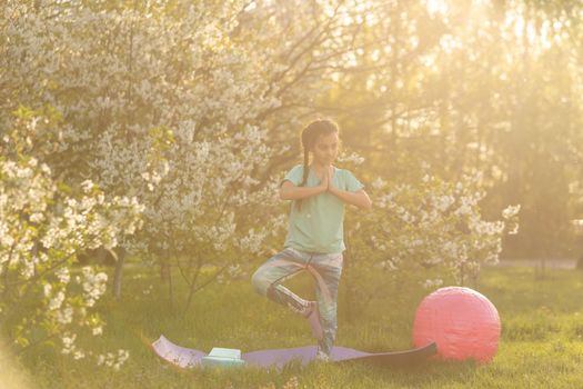 little girl in a T-shirt does yoga on a mat in the garden. a child and a healthy lifestyle.