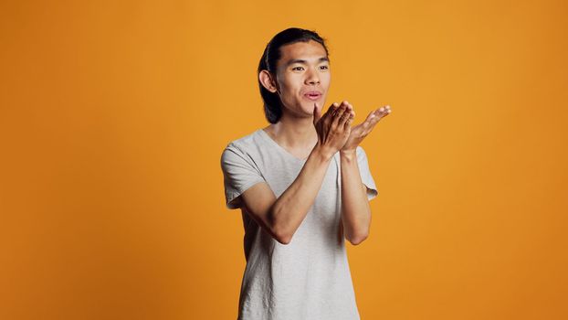 Male model blowing air kisses in studio, acting silly and sensual on orange backdrop. Carefree man sending kisses and being flirty, acting romantic with kissy funny face. Natural confidence.