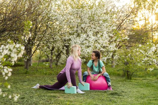 Family Mother teacher training yoga child daughter on a yoga mat at home garden. Family outdoors. Parent with child spends time together. exercise at home concept and new normal