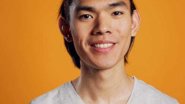 Male model smiling and being carefree on camera, posing over orange backdrop with confidence. Young asian person acting cheerful and friendly in studio, hipster with natural cool style.