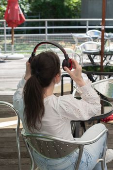 pensive brunette woman in a white blouse, listens to music on headphones at a table in a cafe, High quality photo