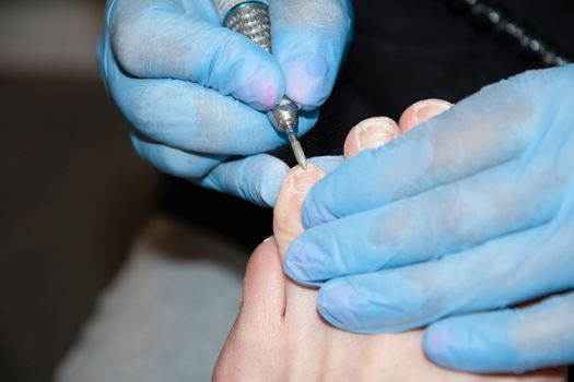 A master in a beauty salon makes a hardware pedicure to a client, Fraser removal of red varnish and cuticles. Close-up, soft focus. High quality photo