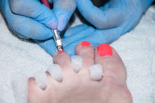 pedicure master paints client's toenails with orange gel polish, foot care in beauty salon, Close-up, soft focus. High quality photo