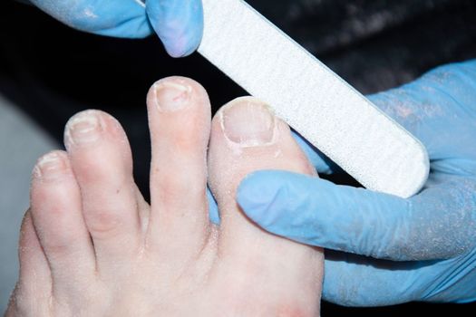 The pedicure master grinds the toenails of clients with a nail file, polishes polishing the nail plate with a buff, High quality photo