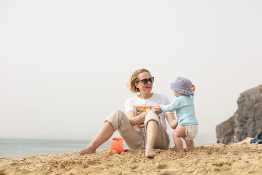 Mother playing his infant baby boy son on sandy beach enjoying summer vacationson on Lanzarote island, Spain. Family travel and vacations concept