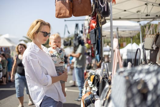 Mother hoding his infant baby boy child whilechecing items at sunday flea market