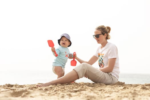 Mother playing his infant baby boy son on sandy beach enjoying summer vacationson on Lanzarote island, Spain. Family travel and vacations concept