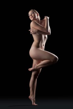 Full length portrait of nude young woman posing in dark studio