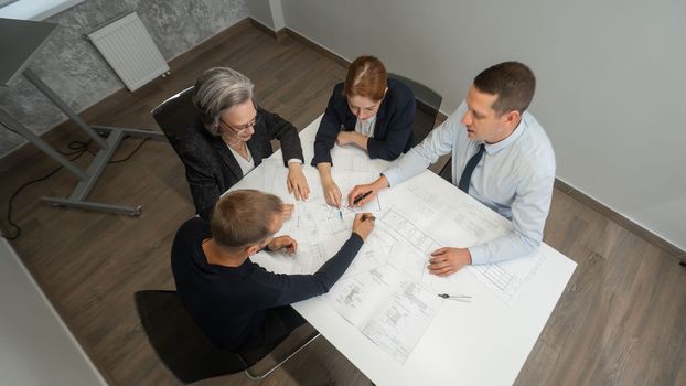 Top view of 4 business people sitting at a table and discussing blueprints. Designers engineers at a meeting