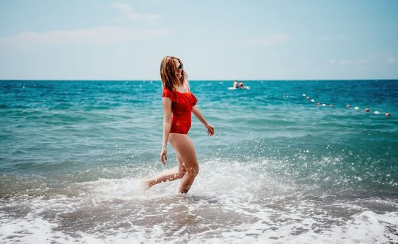 Young happy woman walks carefree on the seaside. Happy lady in red bikini. Portrait beautiful young woman relax smile around beach sea ocean in holiday vacation travel trip.