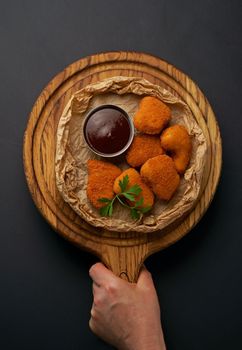 Side view of fried chicken fillet in panko breadcrumbs , sweet and sour sauce in saucepan near dish isolated on black background.