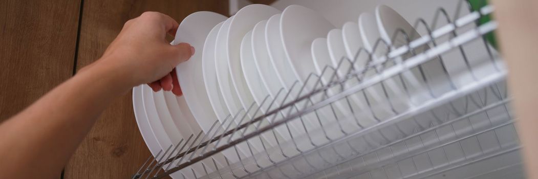 Woman graceful hand takes out clean plate from cupboard. Dryer for dishes in closet concept