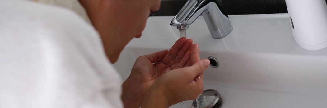 Young woman washes face with clean water in bathroom. Facial skin care concept