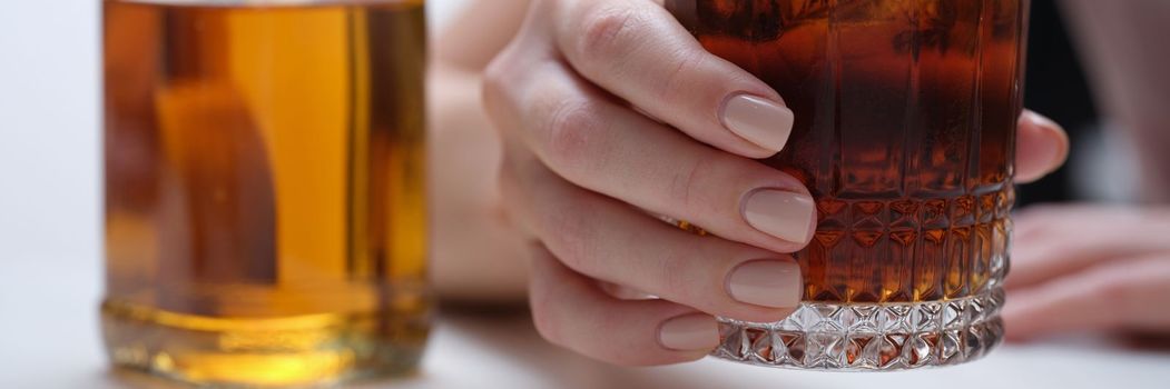 Woman hand holds glass of whiskey or cognac with bottle. Woman suffering from alcohol addiction and depressed woman drinking hard alcohol concept