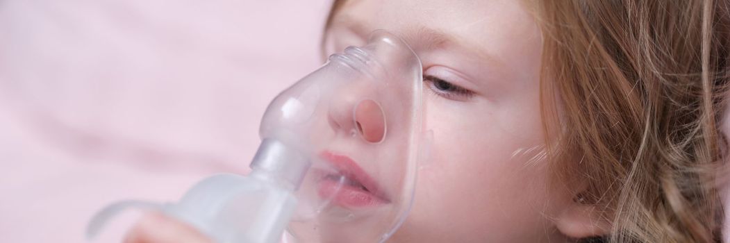 Little baby girl with oxygen mask lying on hospital bed or at home. Upset sad sick child breathing oxygen mask concept