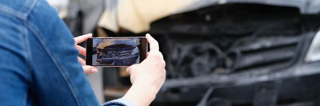 Woman insurance agent or reporter journalist taking pictures of burnt car. Car arson and crime concept