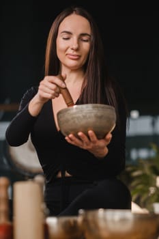 A woman in the lotus position using a singing bowl indoors . Relaxation and meditation. Sound therapy, alternative medicine. Buddhist healing practices.