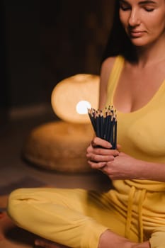 A girl in yellow clothes sitting on the floor holding pencils for drawing.