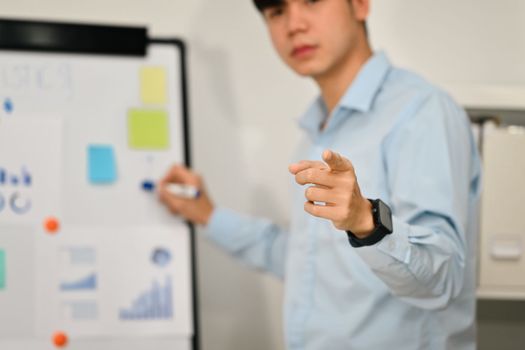 Selective focus, businessman pointing fingers at camera while presenting business data on whiteboard.