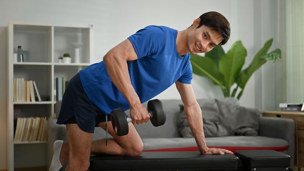 Motivated sportsman exercising with dumbbell at home. Healthy lifestyle and fitness concept.