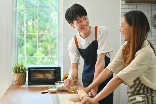 Romantic asian couple preparing homemade pastry on wooden table in kitchen. Love, relationship, people and family.