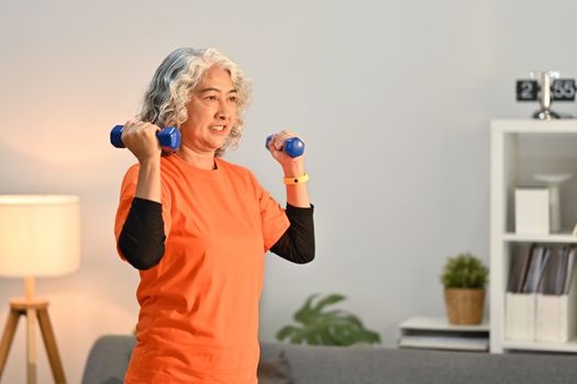Shot of middle aged woman in sport clothes exercising with dumbbells at home. Healthy active lifestyle concept.