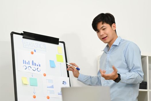 Smiling start up businessman explaining business data on whiteboard during online conference via laptop computer.