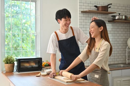 Lovely young asian couple wearing aprons preparing homemade pastry, enjoying leisure time together at home.