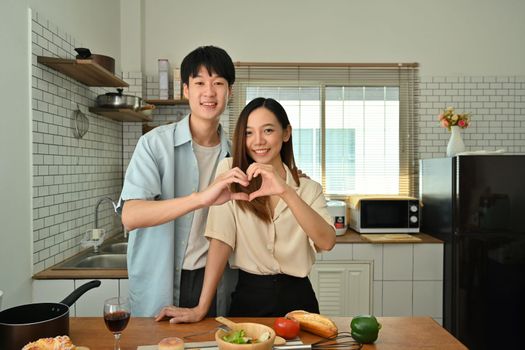 Beautiful young married couple making heart shape with their hands and smiling to camera. Love, relationship and family.