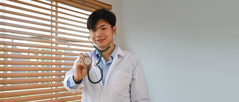 Horizontal banner of doctor in white uniform holding stethoscope and smiling to camera. Healthcare and medical concept.