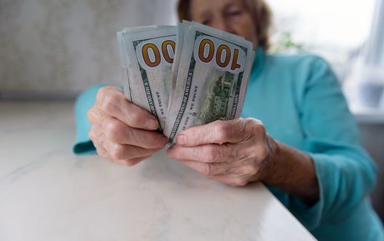 Close-up of an elderly woman's hands holding money in 100 dollar bills, compensation.