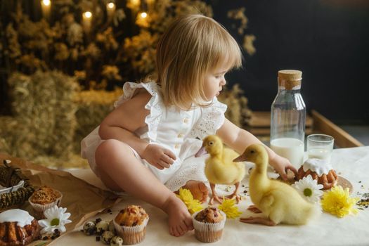 A little girl is sitting on the Easter table and playing with cute fluffy ducklings. The concept of celebrating happy Easter