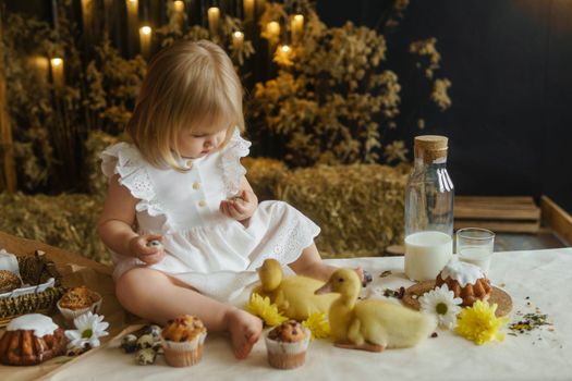 A little girl is sitting on the Easter table and playing with cute fluffy ducklings. The concept of celebrating happy Easter