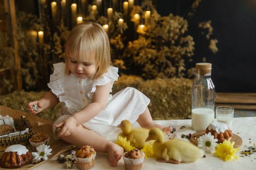 A little girl is sitting on the Easter table and playing with cute fluffy ducklings. The concept of celebrating happy Easter
