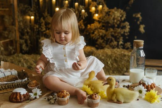 A little girl is sitting on the Easter table and playing with cute fluffy ducklings. The concept of celebrating happy Easter