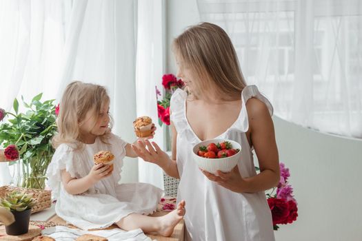 A little blonde girl with her mom on a kitchen countertop decorated with peonies. The concept of the relationship between mother and daughter. Spring atmosphere.