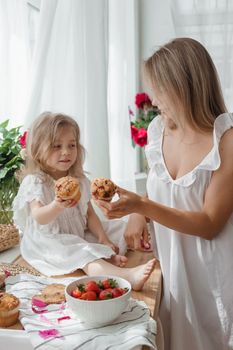 A little blonde girl with her mom on a kitchen countertop decorated with peonies. The concept of the relationship between mother and daughter. Spring atmosphere.