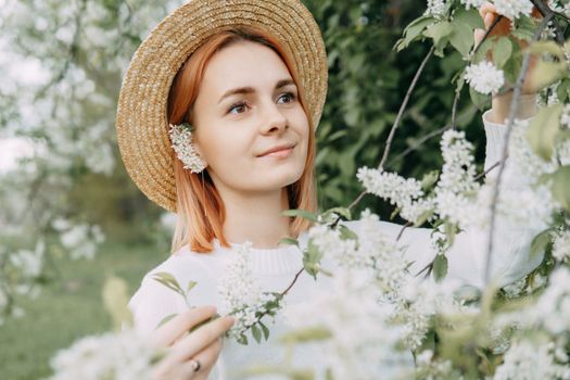 Portrait of a woman in a straw hat in a cherry blossom. Free outdoor recreation, spring blooming garden