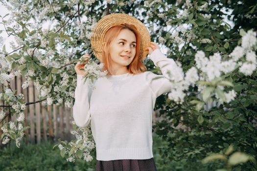 Portrait of a woman in a straw hat in a cherry blossom. Free outdoor recreation, spring blooming garden
