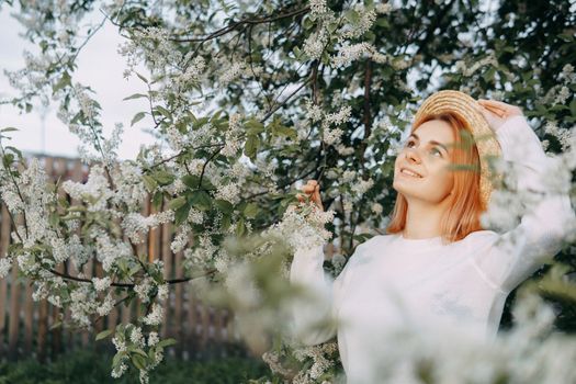 Portrait of a woman in a straw hat in a cherry blossom. Free outdoor recreation, spring blooming garden