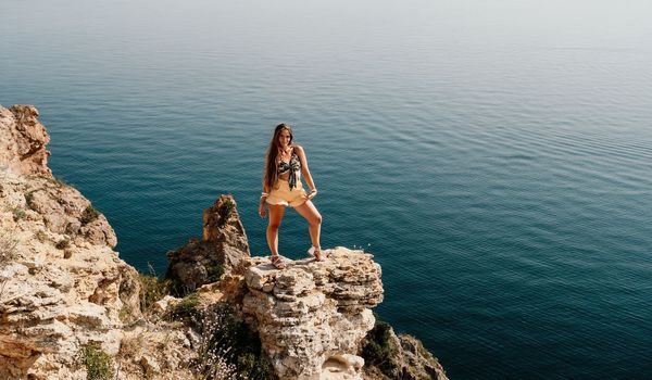 Woman travel sea. Happy tourist taking picture outdoors for memories. Woman traveler looks at the edge of the cliff on the sea bay of mountains, sharing travel adventure journey.