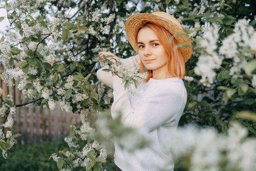 Portrait of a woman in a straw hat in a cherry blossom. Free outdoor recreation, spring blooming garden