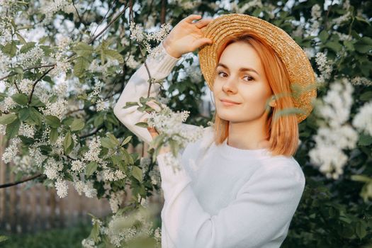 Portrait of a woman in a straw hat in a cherry blossom. Free outdoor recreation, spring blooming garden